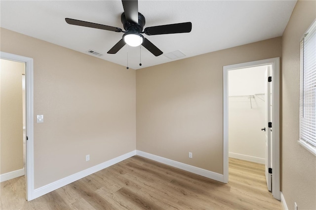 unfurnished bedroom featuring a spacious closet, light hardwood / wood-style floors, a closet, and ceiling fan