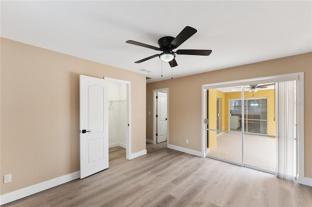 unfurnished bedroom featuring ceiling fan, a closet, light hardwood / wood-style flooring, and a walk in closet