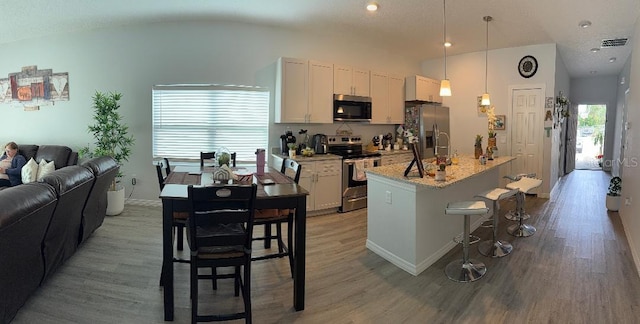 kitchen featuring a breakfast bar, white cabinetry, decorative light fixtures, appliances with stainless steel finishes, and a kitchen island with sink