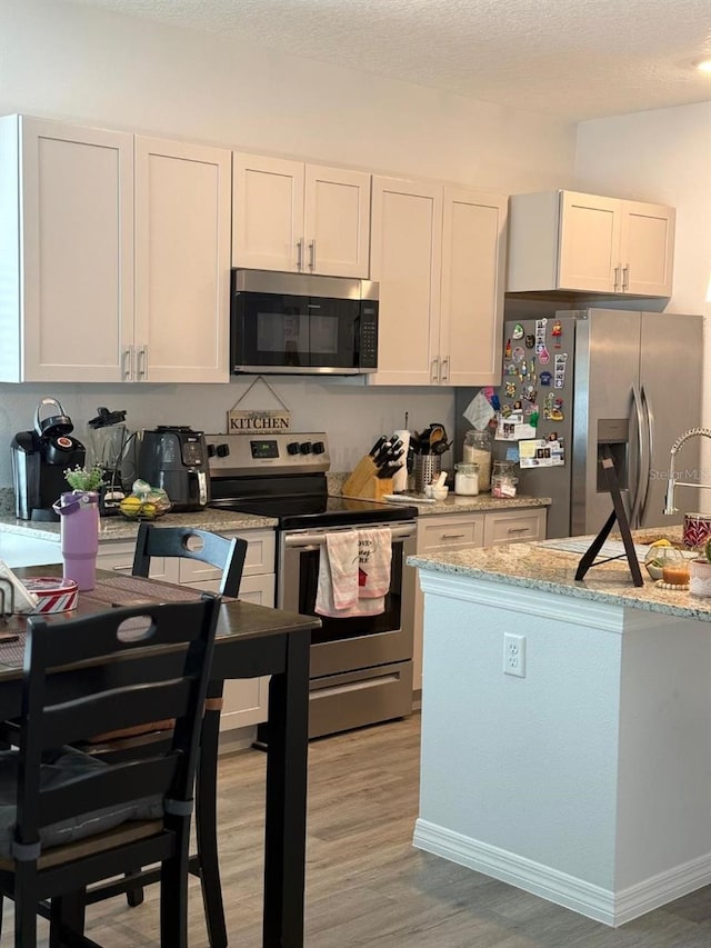 kitchen with a textured ceiling, stainless steel appliances, light wood-style floors, and light stone countertops