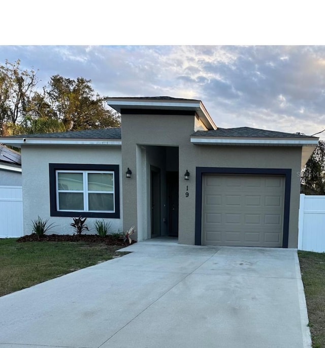 view of front of home featuring concrete driveway, an attached garage, fence, and stucco siding