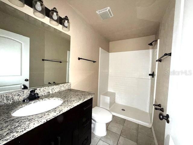 bathroom with tile patterned flooring, vanity, a shower, and toilet