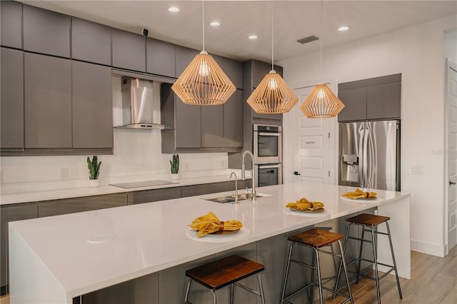 kitchen with appliances with stainless steel finishes, an island with sink, sink, a kitchen bar, and wall chimney exhaust hood