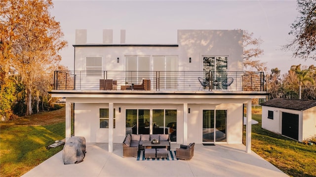 back house at dusk featuring a shed, a lawn, outdoor lounge area, and a balcony