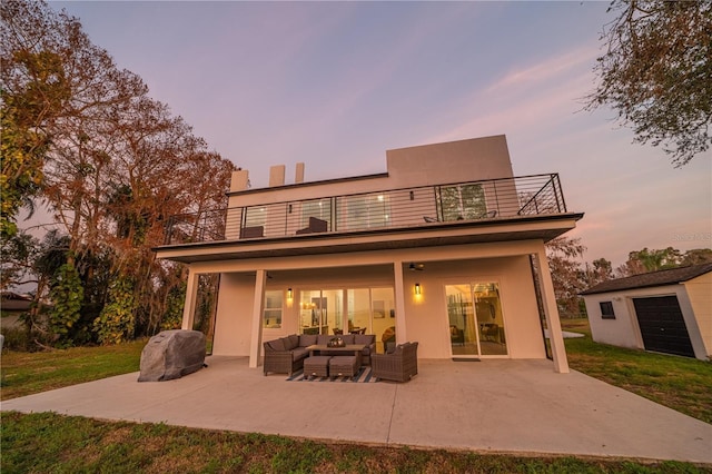 back house at dusk featuring a patio, a balcony, outdoor lounge area, and a shed