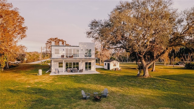 back of property featuring a balcony, a yard, a storage unit, and a patio