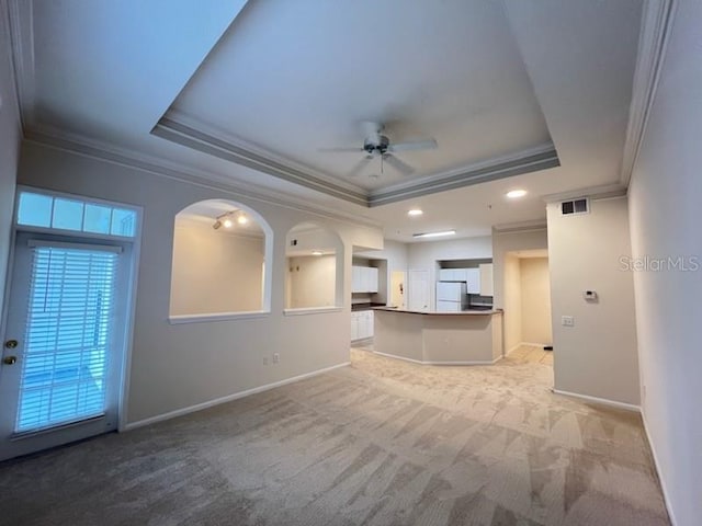 unfurnished living room with light carpet, crown molding, a raised ceiling, and ceiling fan