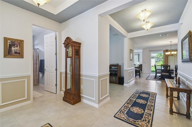 hall with light tile patterned flooring, a chandelier, and a textured ceiling