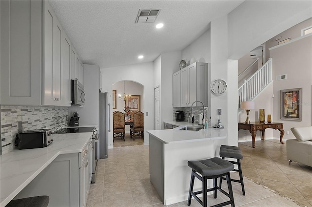 kitchen featuring a kitchen bar, sink, appliances with stainless steel finishes, gray cabinets, and decorative backsplash