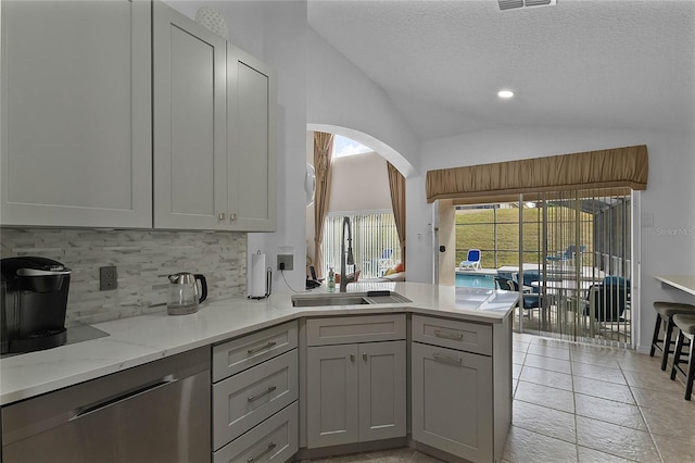 kitchen with sink, gray cabinetry, vaulted ceiling, dishwasher, and backsplash