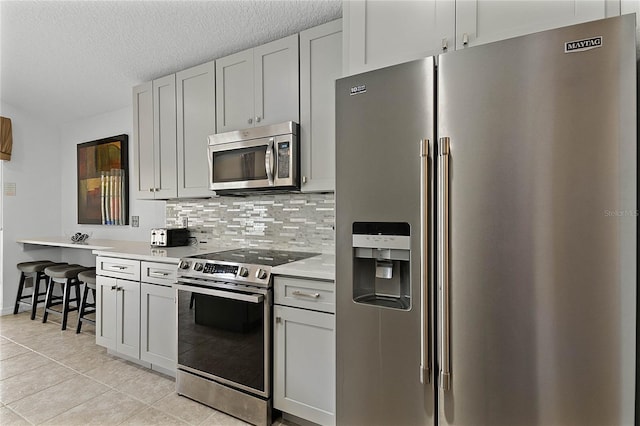 kitchen with stainless steel appliances, a kitchen breakfast bar, tasteful backsplash, a textured ceiling, and light tile patterned flooring