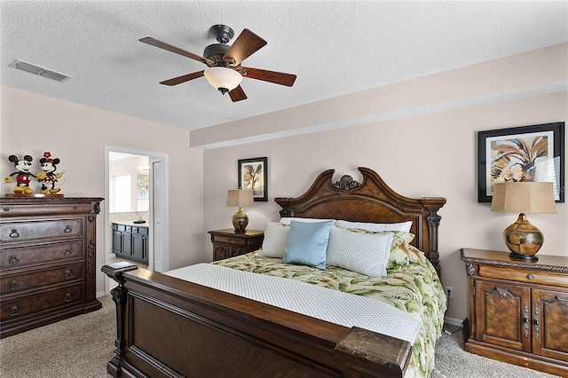 bedroom with ceiling fan, ensuite bath, light carpet, and a textured ceiling