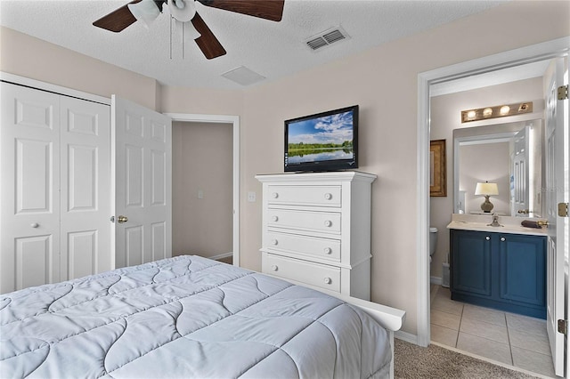 carpeted bedroom featuring ensuite bath, a textured ceiling, a closet, and ceiling fan