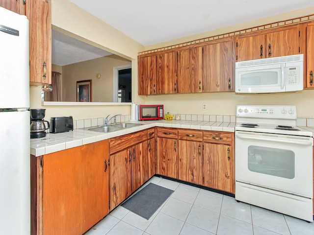 kitchen with light tile patterned floors, white appliances, tile counters, and sink