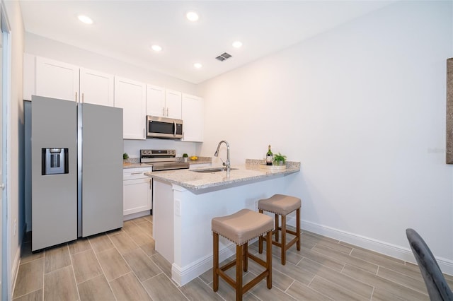 kitchen with sink, white cabinets, a kitchen bar, light stone counters, and stainless steel appliances