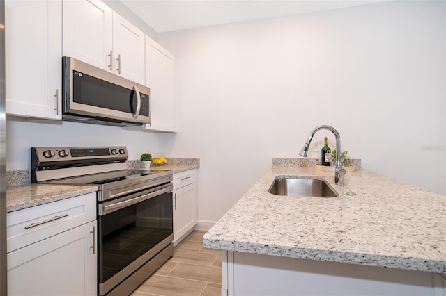 kitchen with white cabinetry, stainless steel appliances, sink, and light stone counters