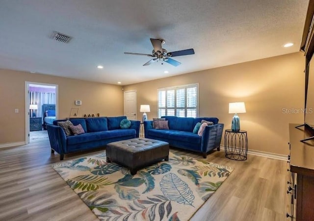 living room featuring ceiling fan, light hardwood / wood-style flooring, and a textured ceiling