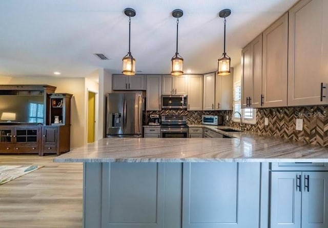 kitchen featuring sink, hanging light fixtures, appliances with stainless steel finishes, kitchen peninsula, and backsplash