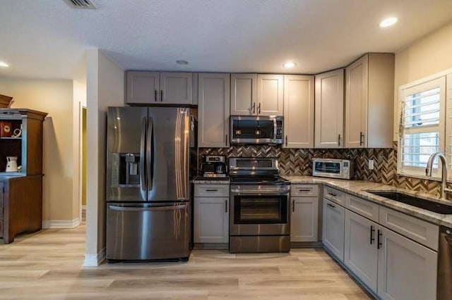 kitchen featuring sink, gray cabinetry, stainless steel appliances, light stone countertops, and decorative backsplash
