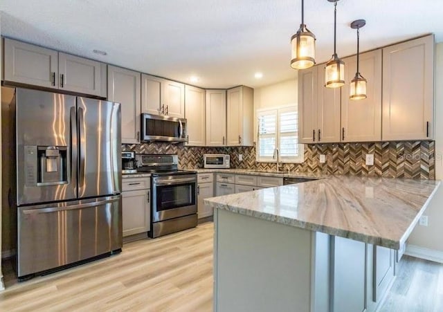 kitchen with gray cabinetry, light stone counters, decorative light fixtures, kitchen peninsula, and stainless steel appliances