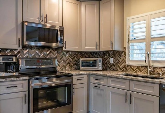 kitchen with appliances with stainless steel finishes, sink, backsplash, and light stone counters