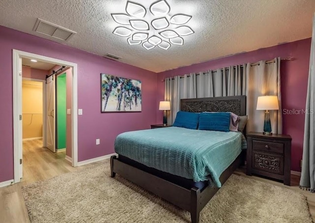 bedroom featuring light hardwood / wood-style flooring, a barn door, and a textured ceiling