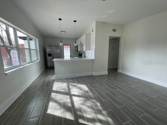 kitchen featuring stainless steel appliances, decorative light fixtures, kitchen peninsula, and white cabinets