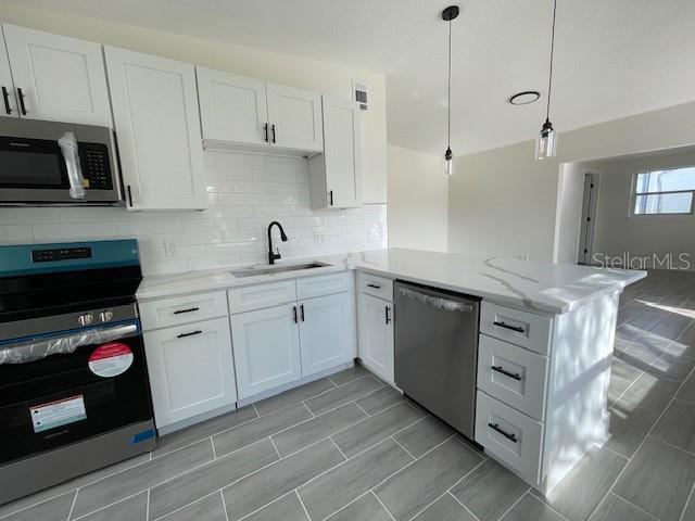 kitchen with sink, stainless steel appliances, white cabinets, decorative light fixtures, and kitchen peninsula