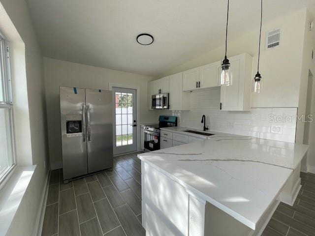 kitchen featuring appliances with stainless steel finishes, pendant lighting, white cabinetry, decorative backsplash, and light stone countertops