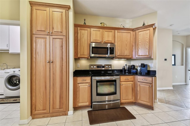 kitchen with dark stone countertops, light tile patterned floors, washer / dryer, and appliances with stainless steel finishes