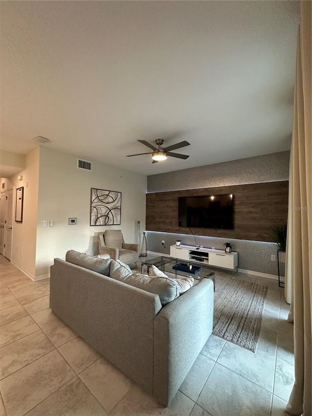 living room featuring baseboards, an accent wall, visible vents, and a ceiling fan