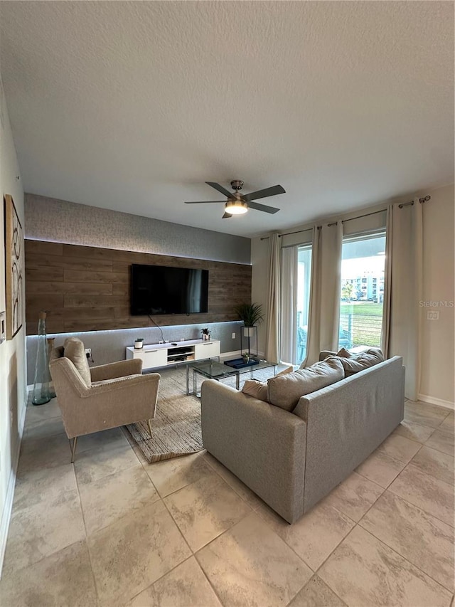 living room featuring a textured ceiling, an accent wall, ceiling fan, and baseboards