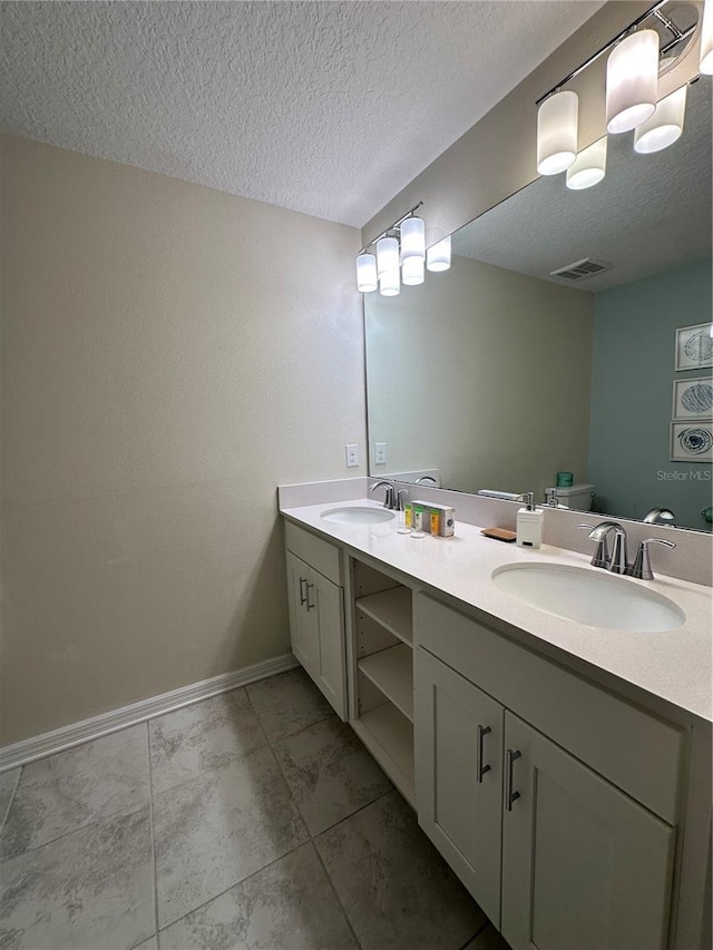 bathroom featuring double vanity, a textured ceiling, visible vents, and a sink