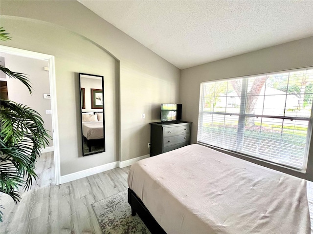 bedroom featuring lofted ceiling, a textured ceiling, and light hardwood / wood-style flooring