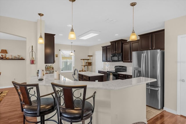 kitchen with light hardwood / wood-style flooring, kitchen peninsula, hanging light fixtures, and black appliances