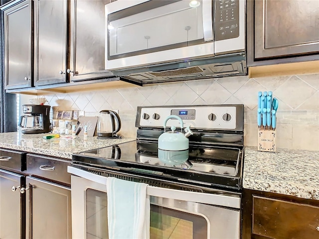 kitchen with dark brown cabinetry, stainless steel appliances, light stone countertops, and decorative backsplash