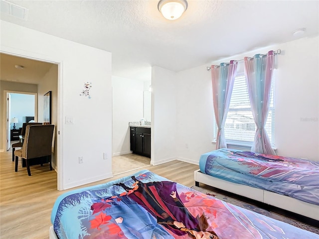 bedroom featuring light wood-type flooring, a textured ceiling, and ensuite bathroom