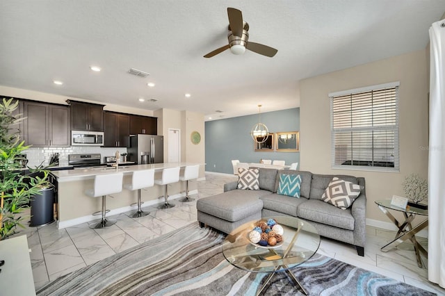 living room featuring sink and ceiling fan with notable chandelier