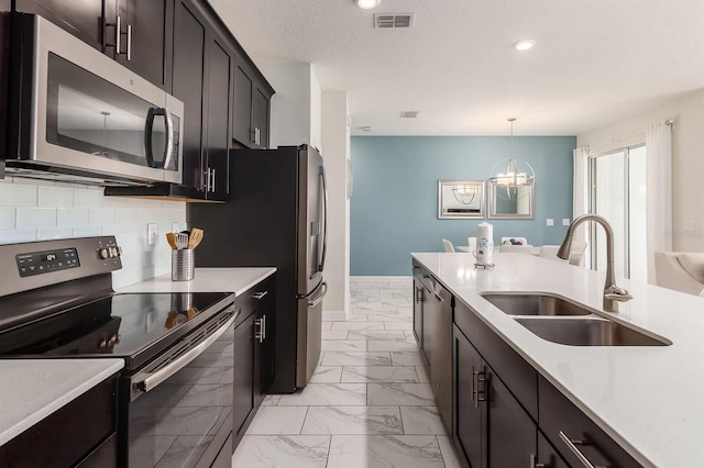 kitchen with appliances with stainless steel finishes, decorative light fixtures, tasteful backsplash, sink, and a textured ceiling