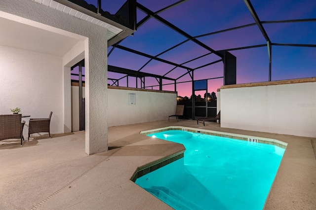 pool at dusk featuring a patio and glass enclosure