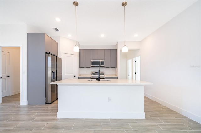 kitchen with stainless steel appliances, hanging light fixtures, a kitchen island with sink, and gray cabinetry