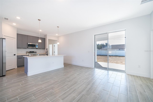 kitchen with sink, gray cabinets, hanging light fixtures, stainless steel appliances, and an island with sink