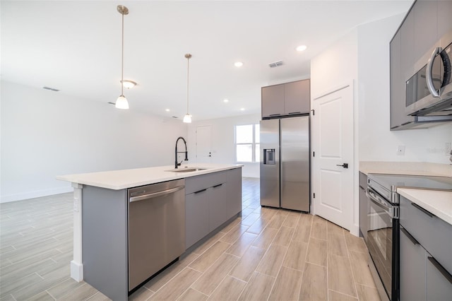 kitchen with sink, gray cabinetry, hanging light fixtures, an island with sink, and stainless steel appliances