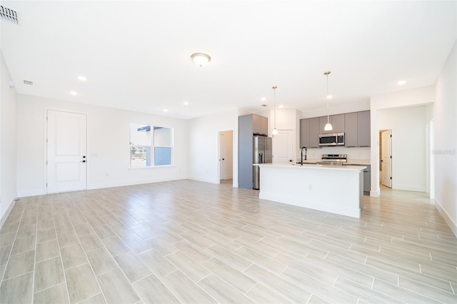 kitchen with gray cabinets, appliances with stainless steel finishes, decorative light fixtures, an island with sink, and sink