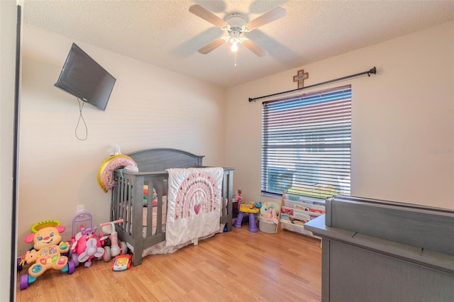 bedroom featuring hardwood / wood-style floors, a nursery area, a textured ceiling, and ceiling fan