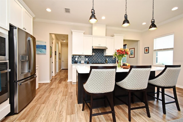 kitchen with pendant lighting, a kitchen island with sink, white cabinets, and appliances with stainless steel finishes