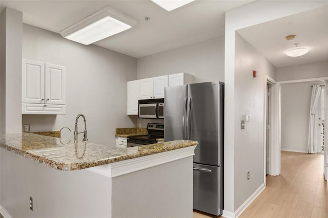 kitchen with appliances with stainless steel finishes, white cabinets, light stone counters, and kitchen peninsula