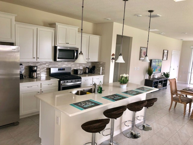 kitchen with pendant lighting, sink, stainless steel appliances, white cabinets, and a kitchen bar