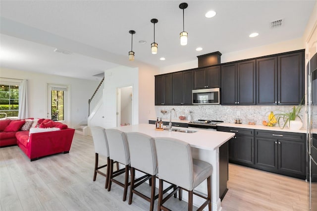 kitchen with sink, decorative light fixtures, appliances with stainless steel finishes, a kitchen island with sink, and backsplash