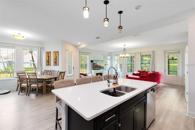 kitchen with sink, dishwasher, hanging light fixtures, a center island with sink, and light wood-type flooring